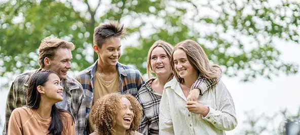 A group of teenagers smile and hold each other while outdoors on a sunny day